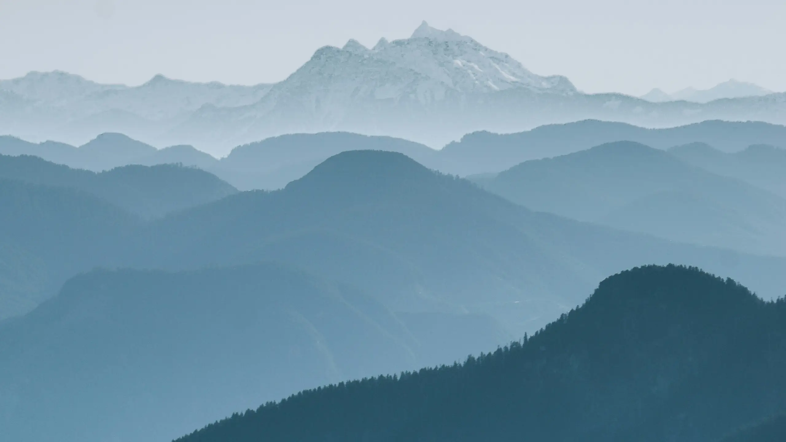 Layered blue mountain ridges fading into mist beneath a snow-capped peak
